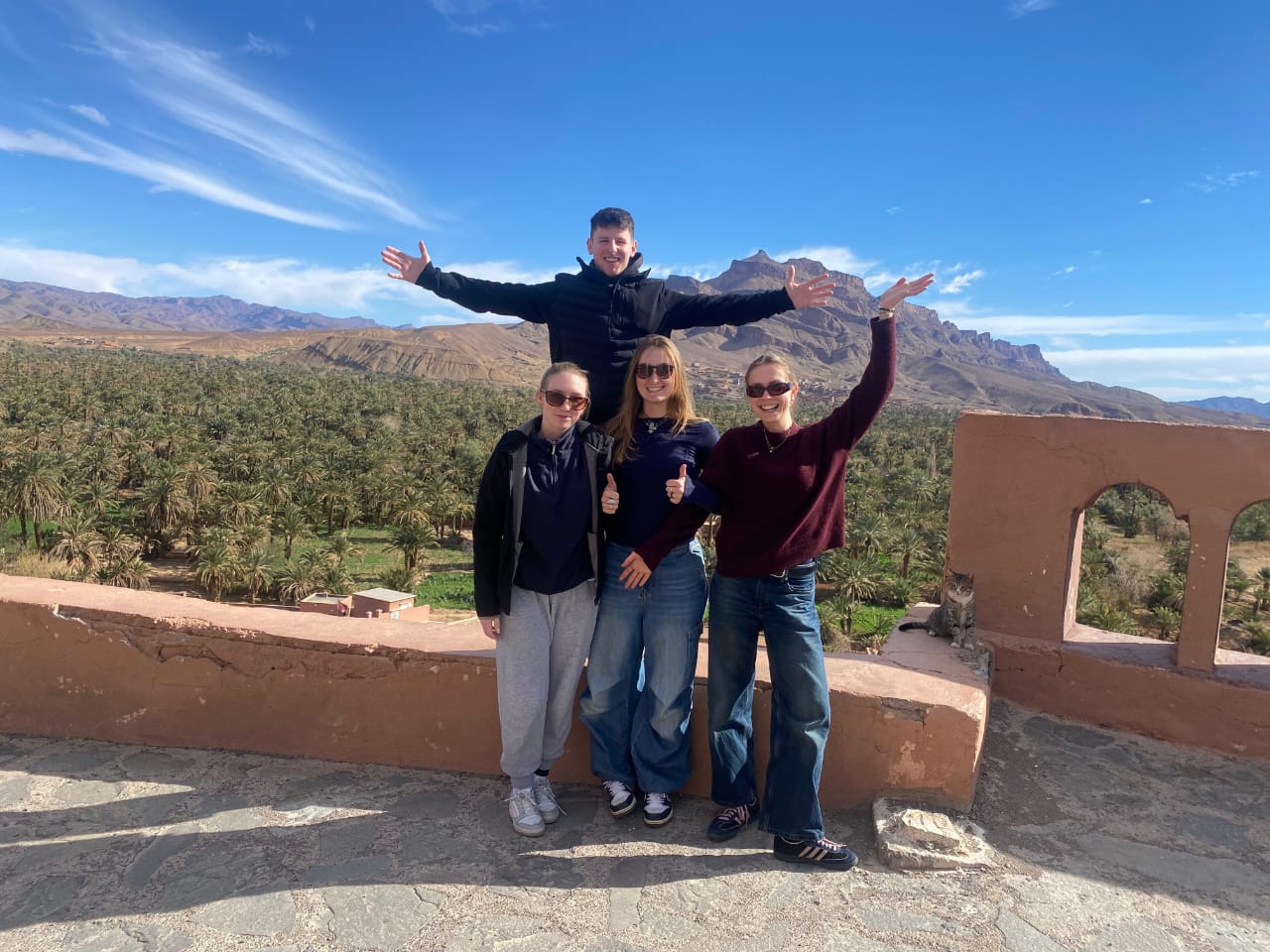 Travelers on a rooftop terrace overlooking the Ounila Valley palm oasis near Ait Ben Haddou