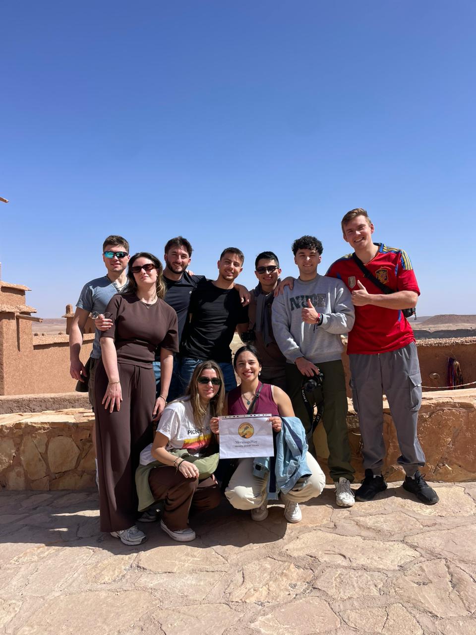 MerzougaWay travelers holding the MerzougaWay tour sign at Kasbah Ait Ben Haddou